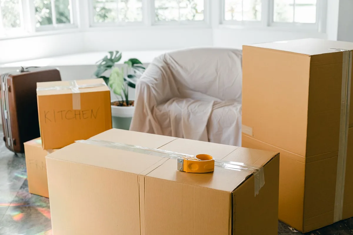 Sealed cardboard boxes stacked in a bright room beside a covered armchair